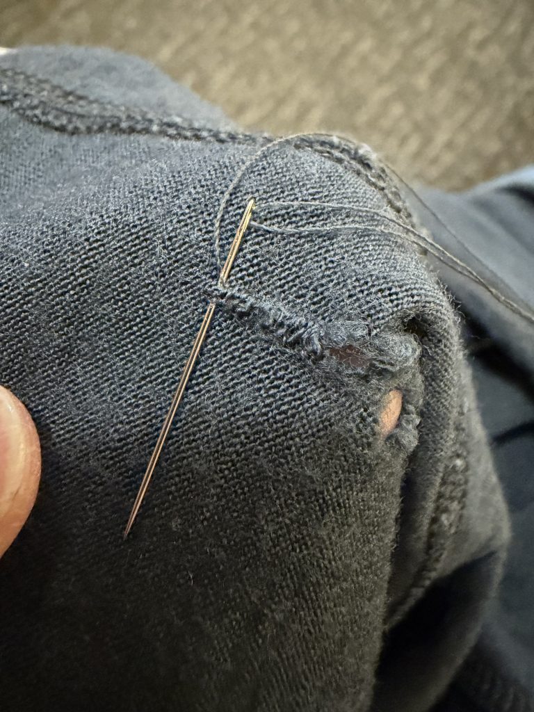 A close up photo of a needle and thread mending a small hole in a knit shirt. 